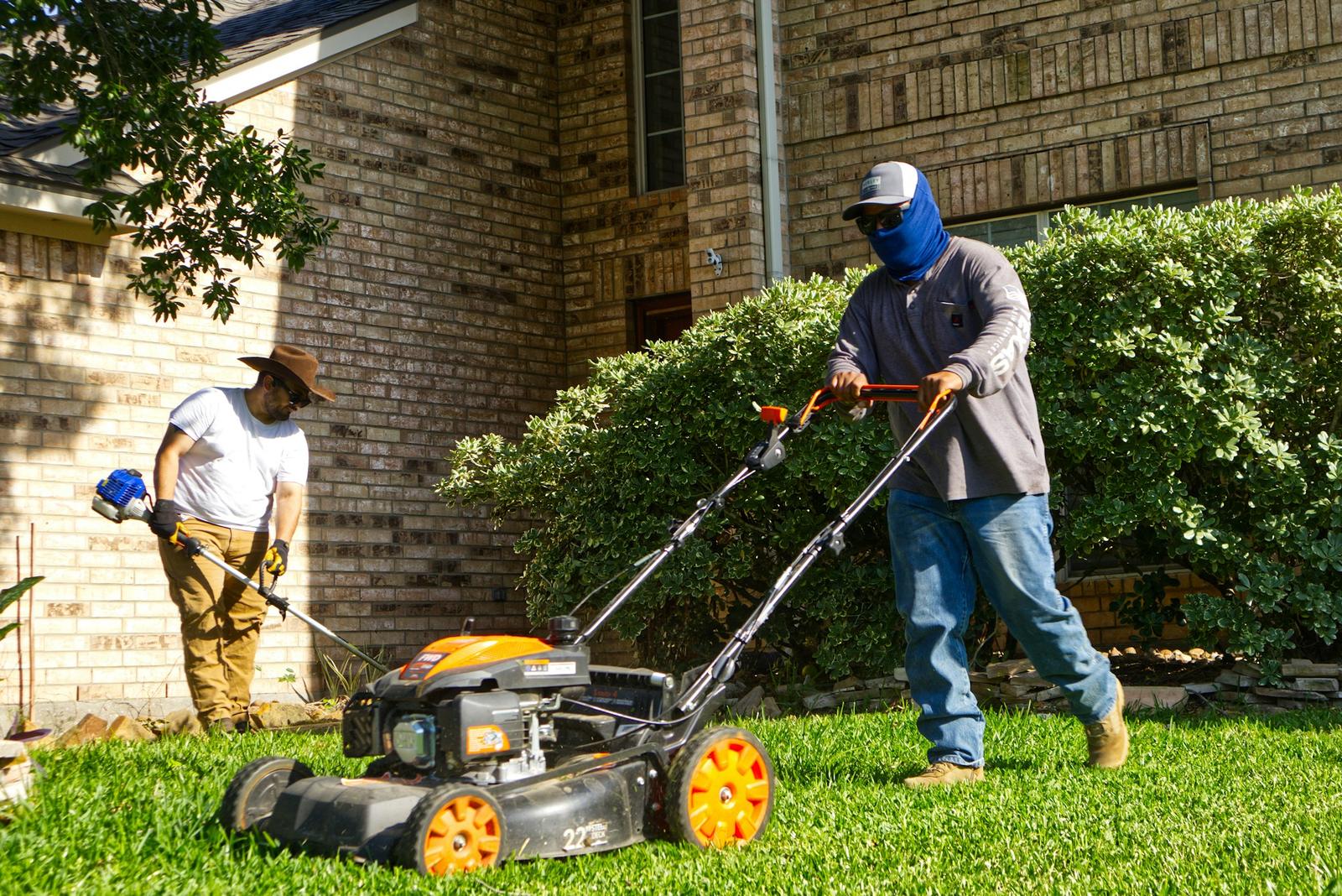 Two lawn crew members mowing and trimming a front yard